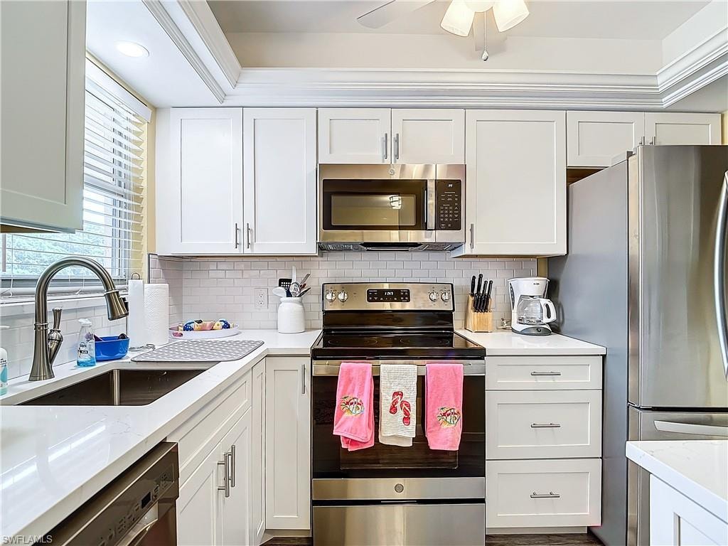 Kitchen with sink, white cabinetry, appliances with stainless steel finishes, decorative backsplash, and ceiling fan