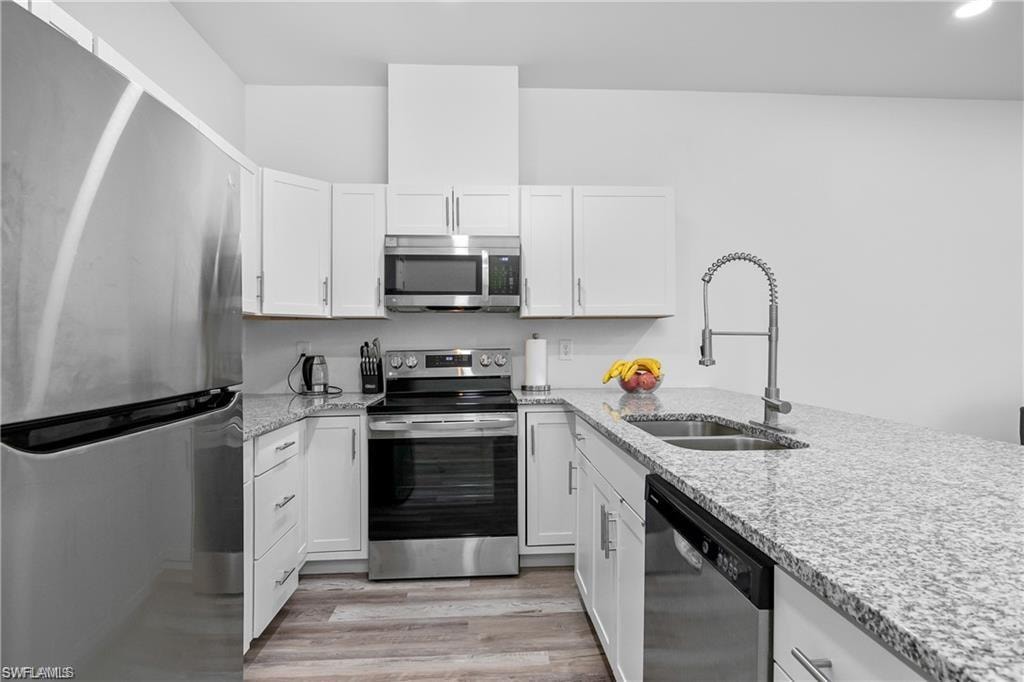 Kitchen featuring appliances with stainless steel finishes, light stone countertops, and white cabinets