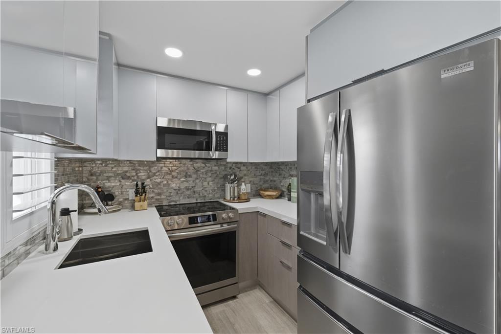 Kitchen featuring modern cabinets, appliances with stainless steel finishes, tasteful backsplash, recessed lighting, and white cabinetry