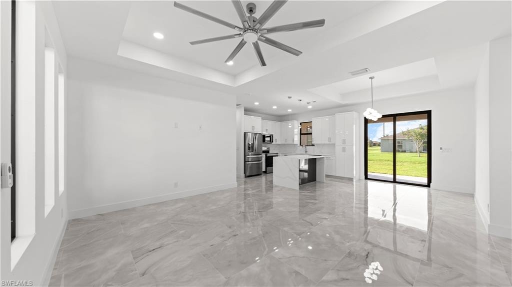 Unfurnished living room featuring a raised ceiling, light marble finish flooring, recessed lighting, and a ceiling fan