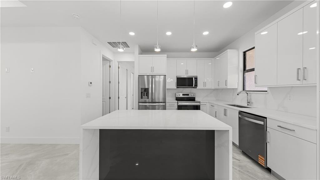 Kitchen featuring white cabinets, appliances with stainless steel finishes, pendant lighting, a kitchen island, and recessed lighting
