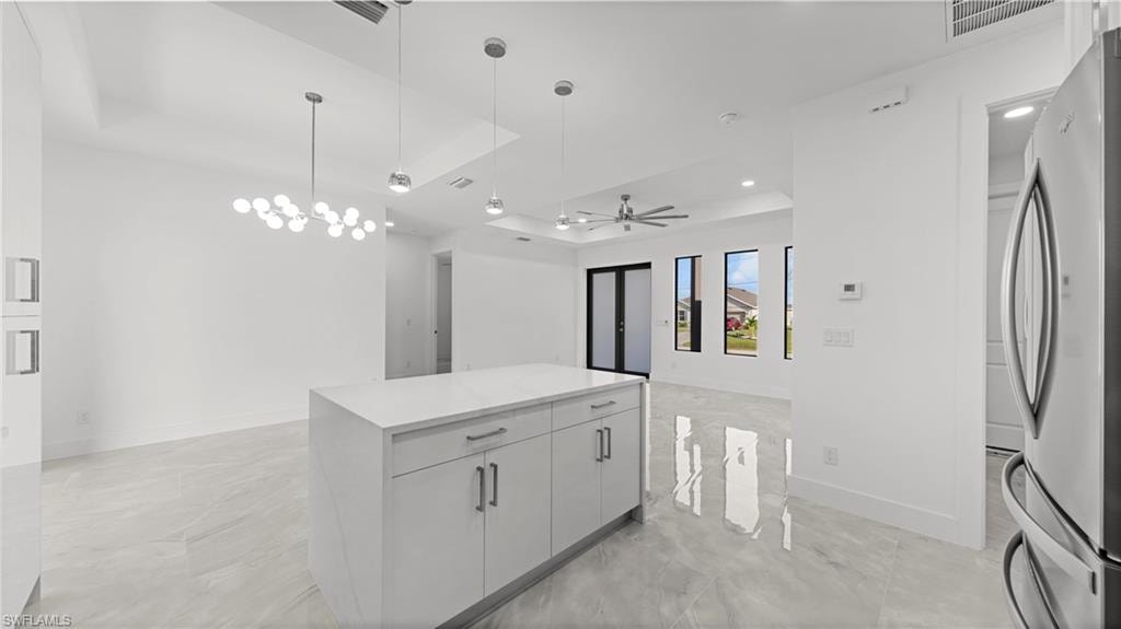 Kitchen with a tray ceiling, hanging light fixtures, freestanding refrigerator, a ceiling fan, and a kitchen island
