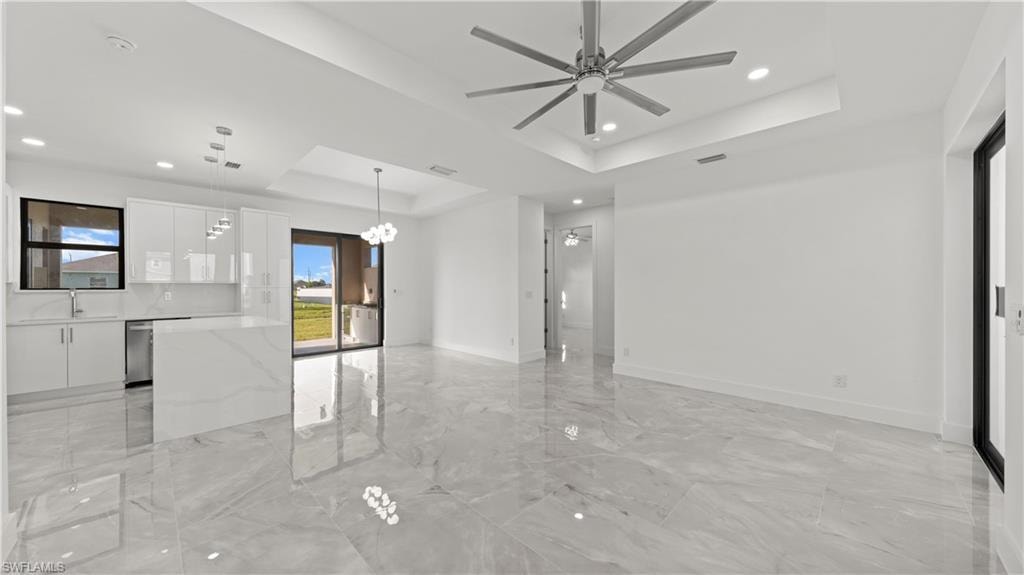 Spare room featuring a tray ceiling, light marble finish flooring, a chandelier, a ceiling fan, and recessed lighting