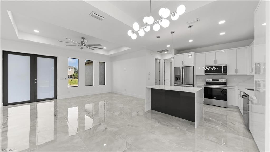 Kitchen featuring white cabinetry, a center island, stainless steel appliances, decorative light fixtures, and open floor plan