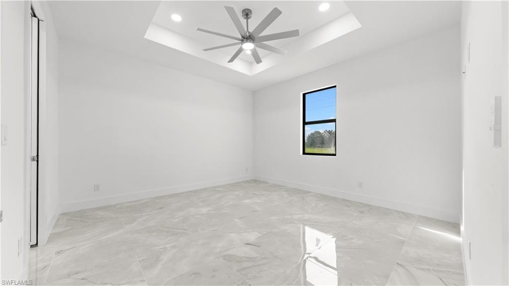 Spare room featuring a tray ceiling, recessed lighting, light marble finish flooring, and a ceiling fan