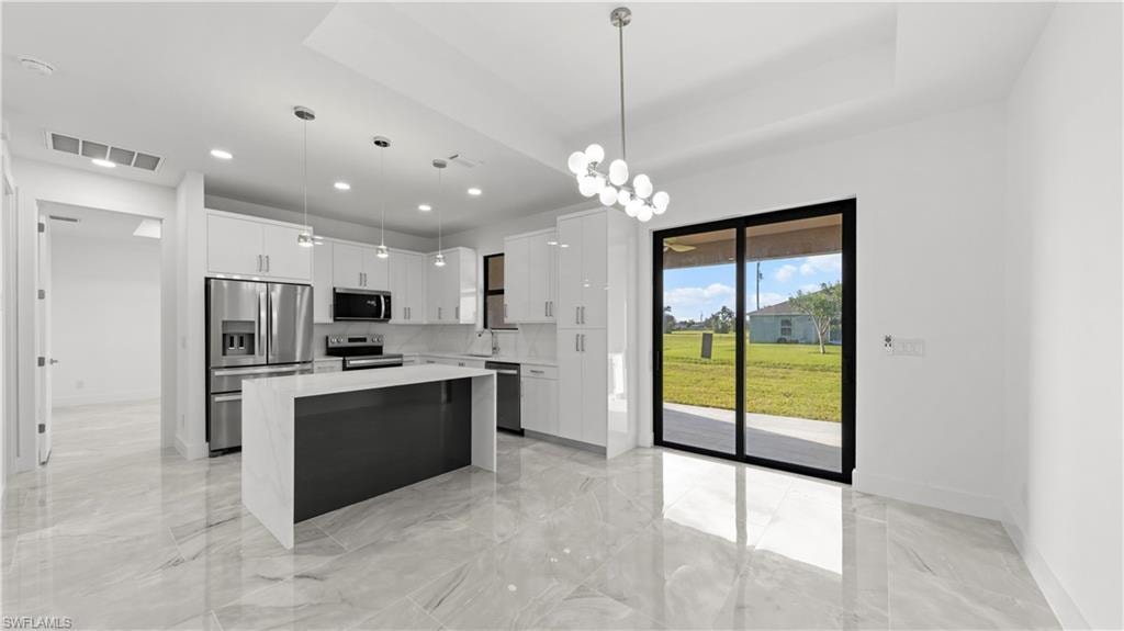 Kitchen with a center island, appliances with stainless steel finishes, white cabinets, pendant lighting, and a chandelier