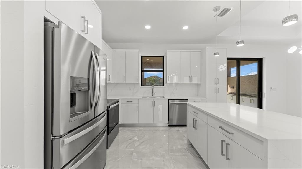 Kitchen featuring appliances with stainless steel finishes, light marble finish floors, decorative light fixtures, white cabinets, and recessed lighting