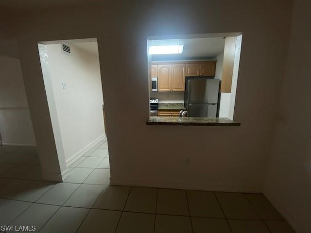 Kitchen with stove, light brown cabinets, sink, refrigerator, and light tile patterned flooring