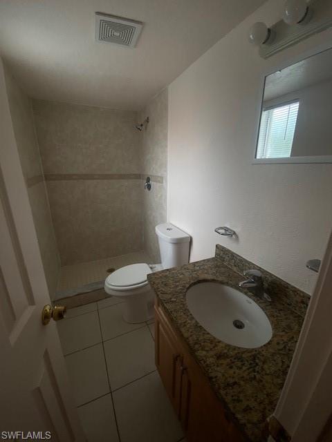 Bathroom featuring tiled shower, vanity, tile patterned floors, and toilet