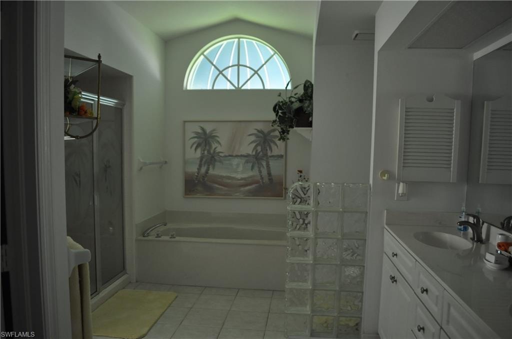 Full bath featuring vanity, a bath, a shower stall, light tile patterned floors, and vaulted ceiling
