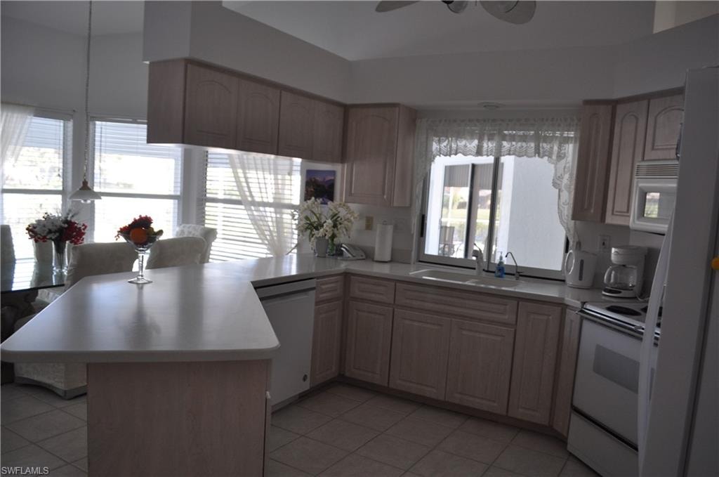 Kitchen with white appliances, a peninsula, light countertops, light tile patterned flooring, and a ceiling fan