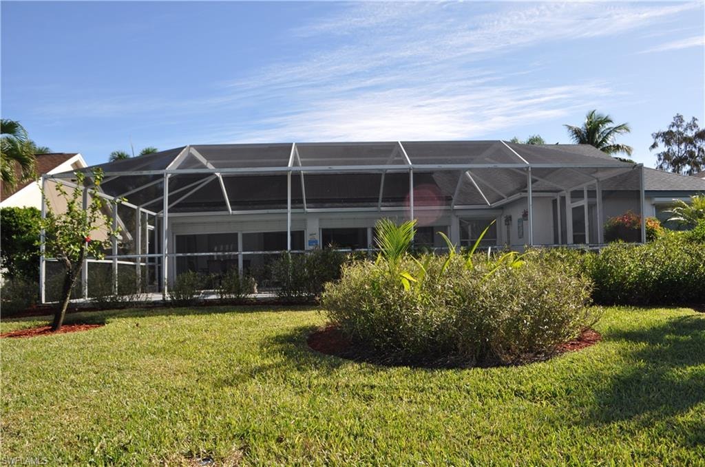 Back of property featuring a sunroom, glass enclosure, and a lawn