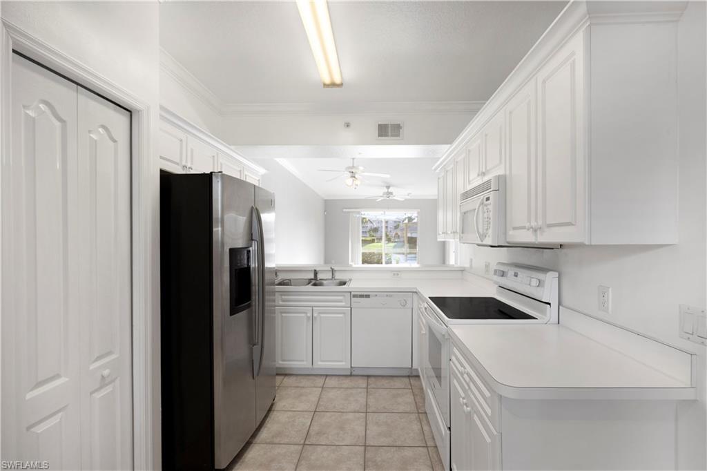 Kitchen featuring white appliances, white cabinetry, light tile patterned flooring, light countertops, and ornamental molding
