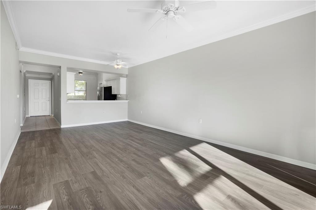 Unfurnished living room featuring crown molding, dark wood-style floors, and a ceiling fan