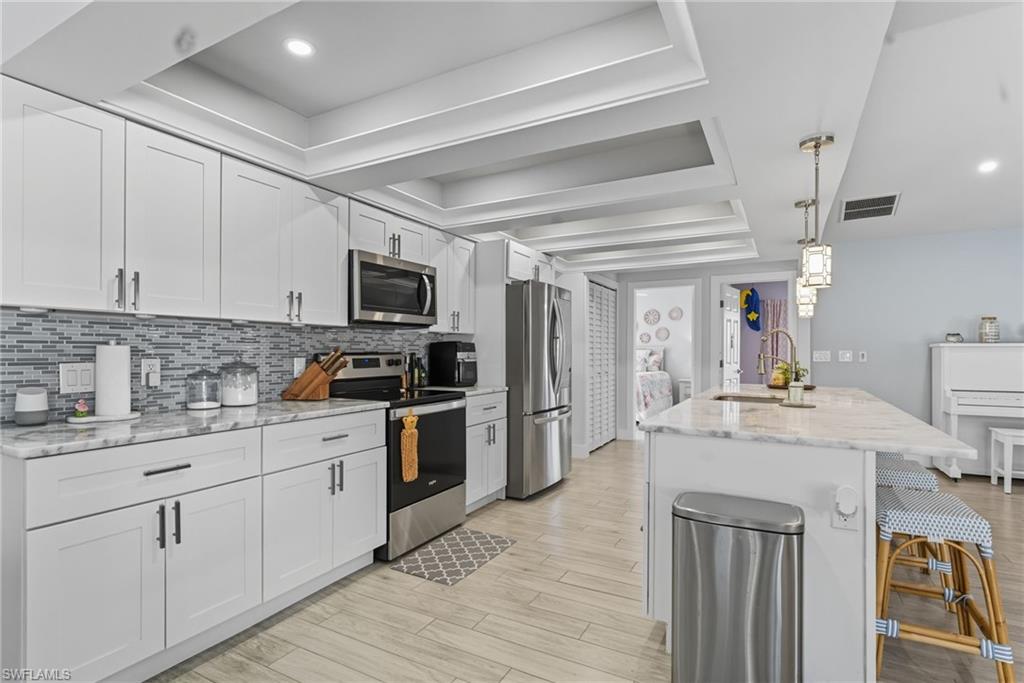 Kitchen with a tray ceiling, stainless steel appliances, light stone countertops, decorative light fixtures, and a kitchen breakfast bar