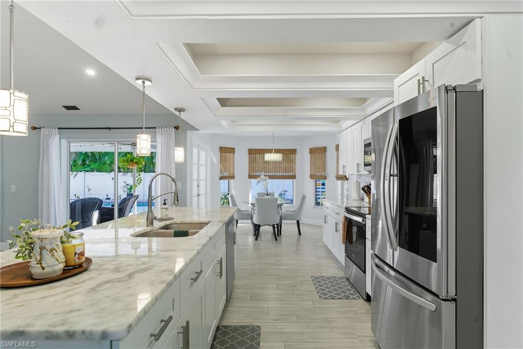 Kitchen featuring stainless steel appliances, white cabinetry, light stone countertops, and decorative light fixtures