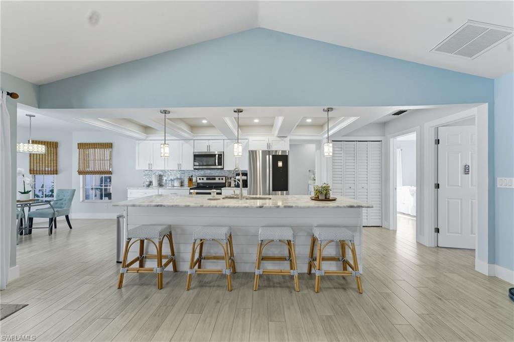 Kitchen featuring white cabinets, stainless steel appliances, light stone counters, decorative backsplash, and a breakfast bar area