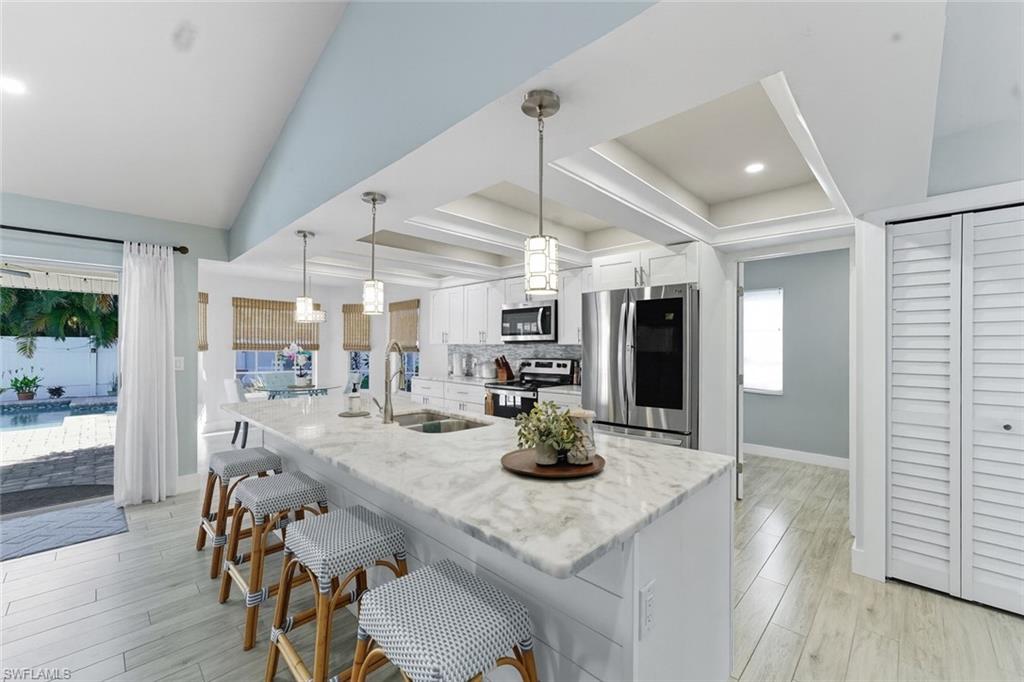 Kitchen with white cabinetry, appliances with stainless steel finishes, a breakfast bar, light stone counters, and light wood-style floors