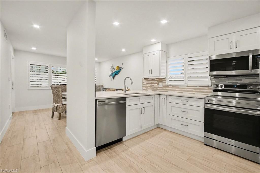 Kitchen featuring stainless steel appliances, white cabinetry, a tiled backsplash, recessed lighting, and wood-finish flooring