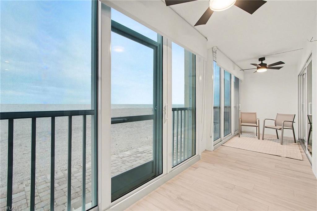 Expansive outdoor balcony featuring large sliding glass doors, light wood-finish flooring, and black ceiling fans