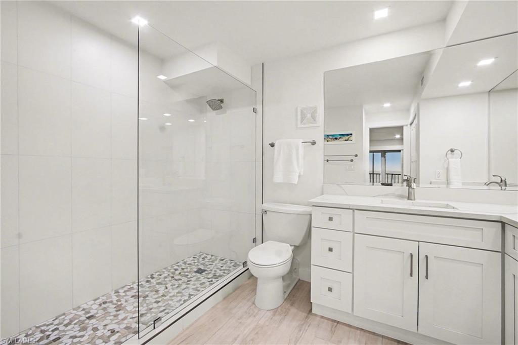 Bathroom featuring a frameless glass shower enclosure with pebble floor, white wall tile, and a rainfall shower head