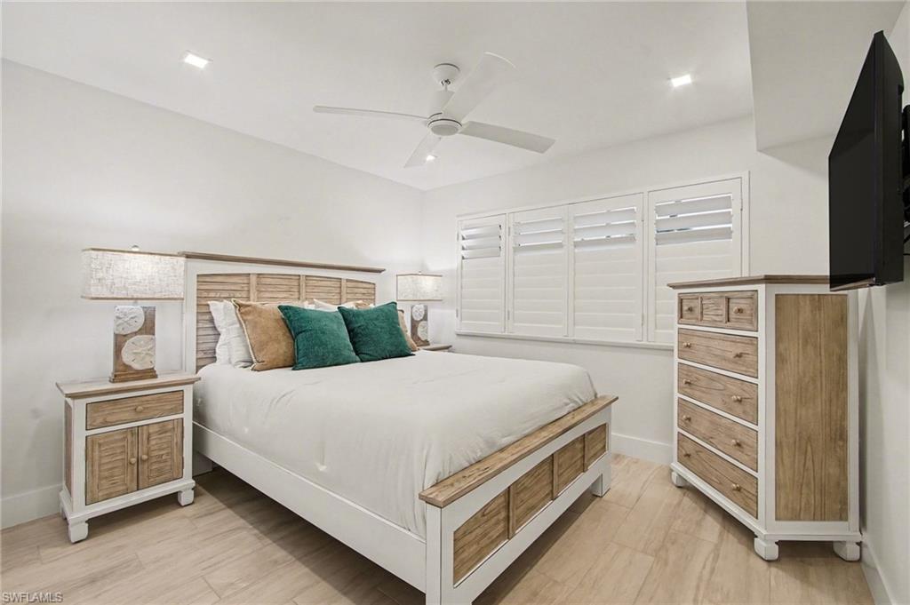 Spacious bedroom featuring light wood-finish flooring, recessed lighting, ceiling fan, and white plantation shutters