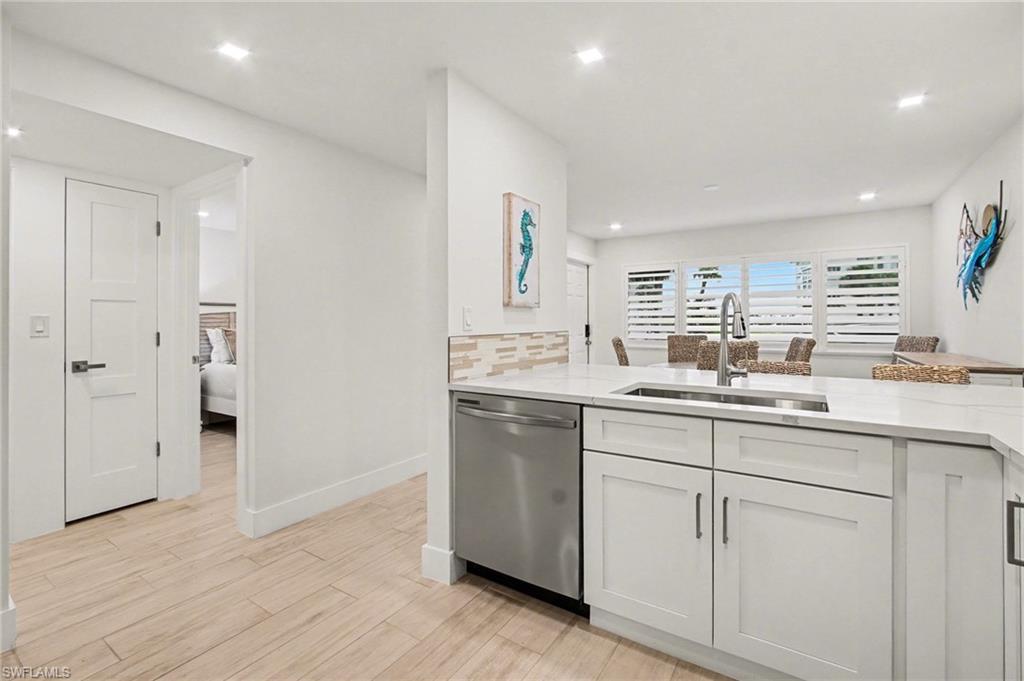 Contemporary kitchen island with a stainless steel undermount sink, gooseneck faucet, white shaker cabinetry, stainless steel dishwasher, and light-toned tile backsplash
