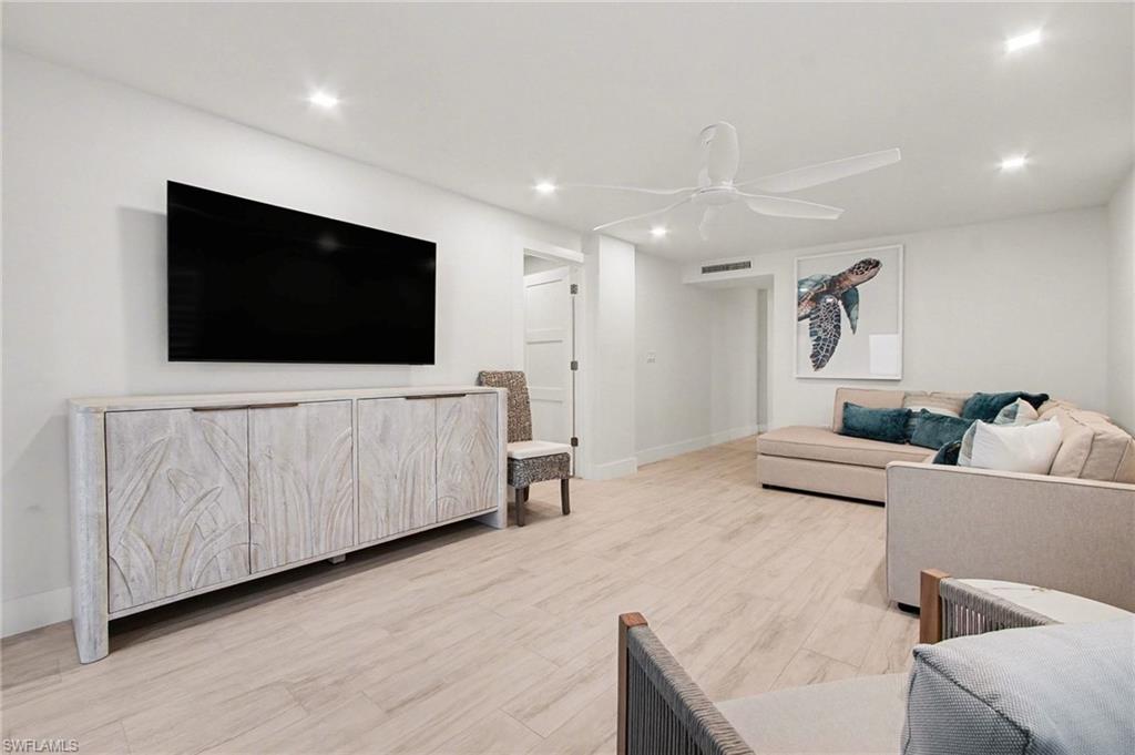 Recessed lighting illuminates an entertainment space featuring wood-finish flooring and a white ceiling fan
