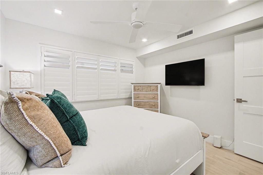 Well-lit interior space featuring recessed lighting, a ceiling fan, light wood-finish flooring, white plantation shutters, and a modern white door with a minimalist handle