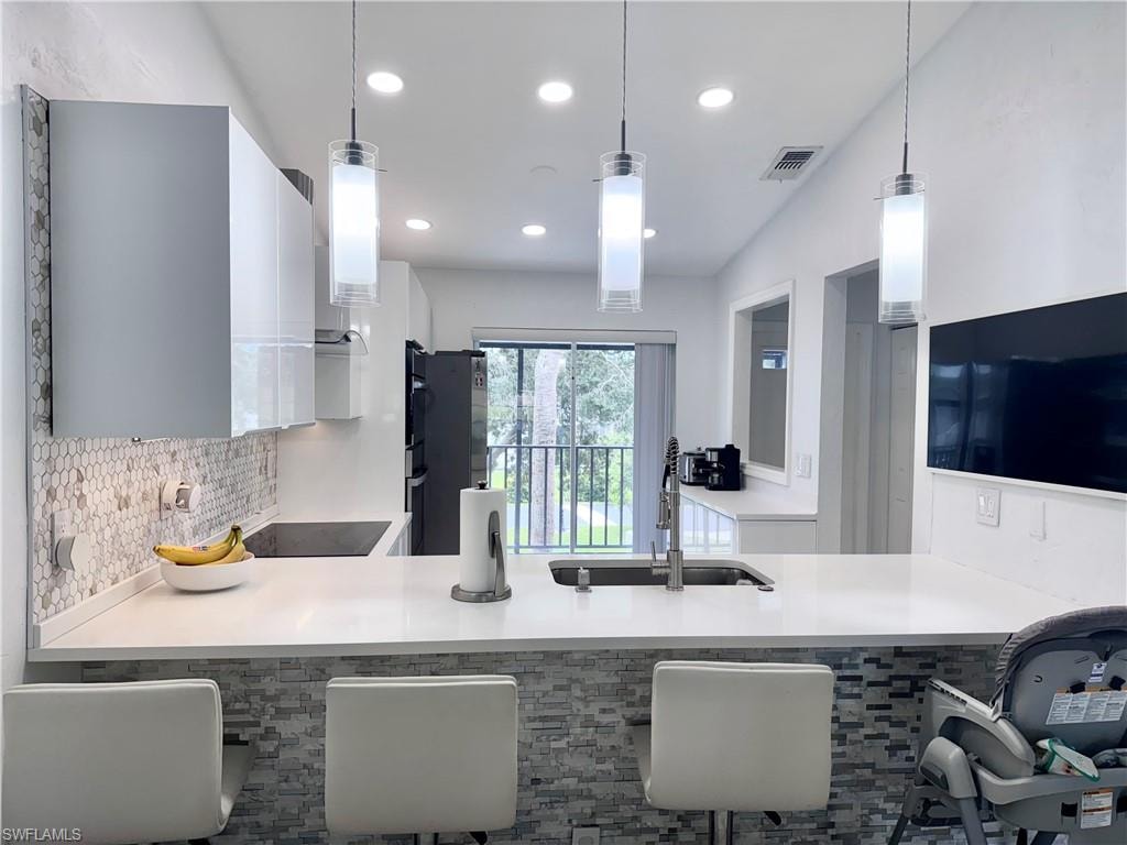 Kitchen with white cabinetry, a peninsula, hanging light fixtures, black electric cooktop, and modern cabinets