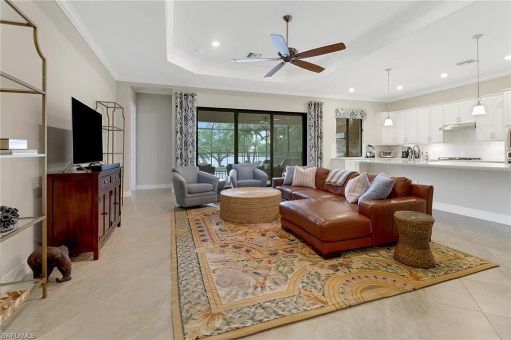 Tiled great room featuring tray ceiling, ceiling fan, and sliding glass door leading to the lanai