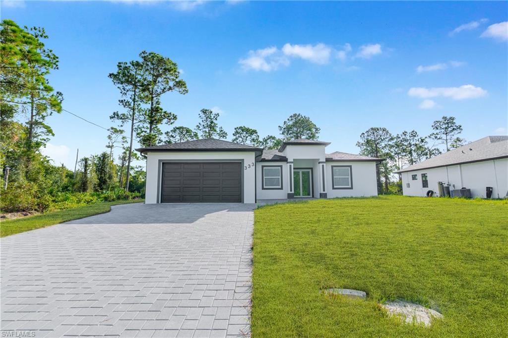 Prairie-style home with decorative driveway, a front lawn, an attached garage, and stucco siding