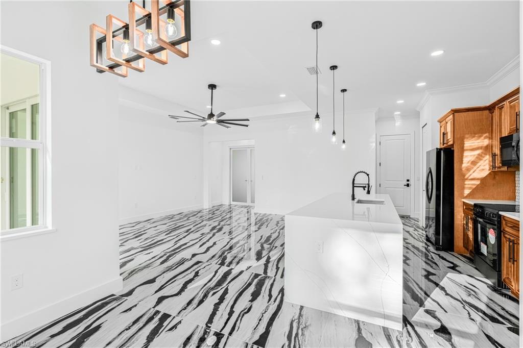 Kitchen featuring decorative light fixtures, black appliances, recessed lighting, brown cabinets, and a center island with sink