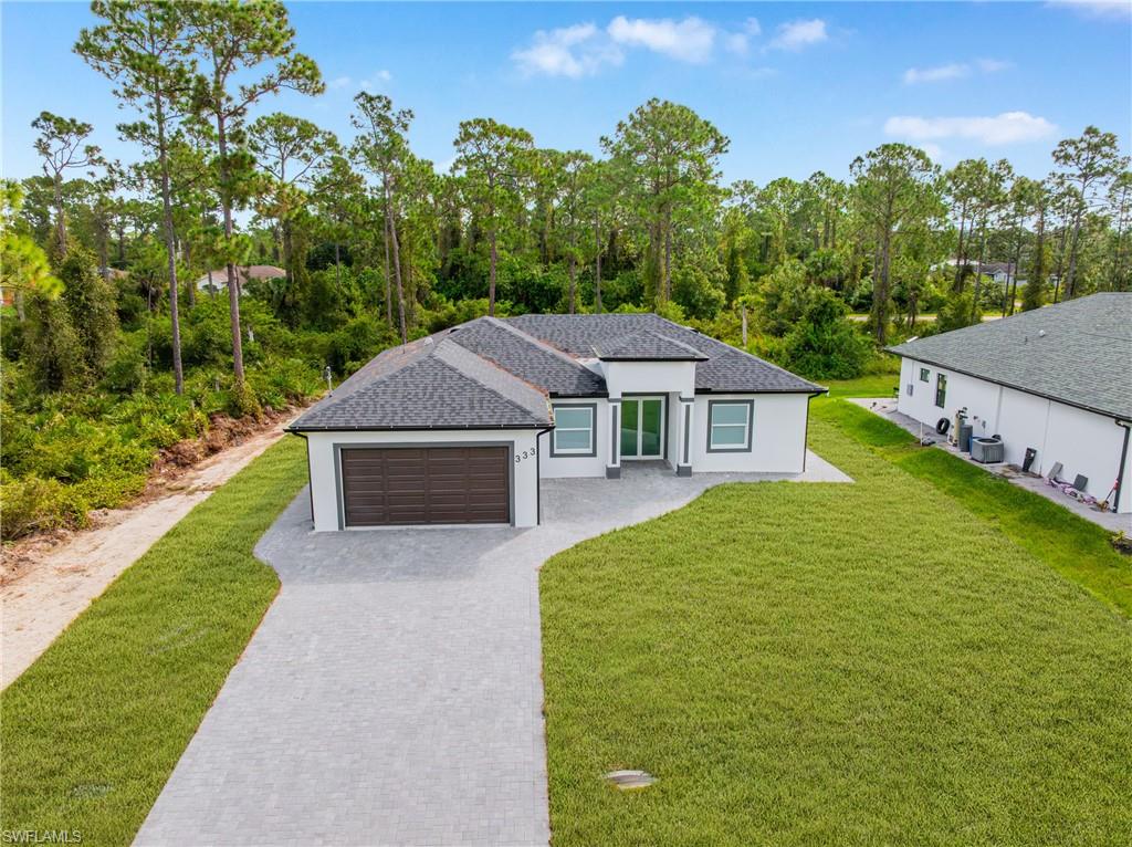View of front of home with a front lawn, decorative driveway, an attached garage, a shingled roof, and stucco siding