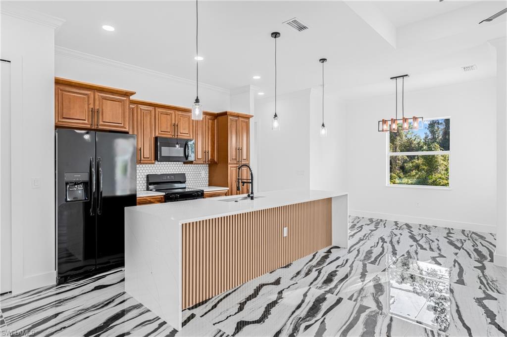 Kitchen featuring brown cabinets, black appliances, tasteful backsplash, light marble finish flooring, and pendant lighting