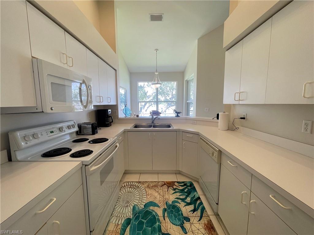 Kitchen with white appliances, light countertops, light tile patterned flooring, decorative light fixtures, and white cabinets