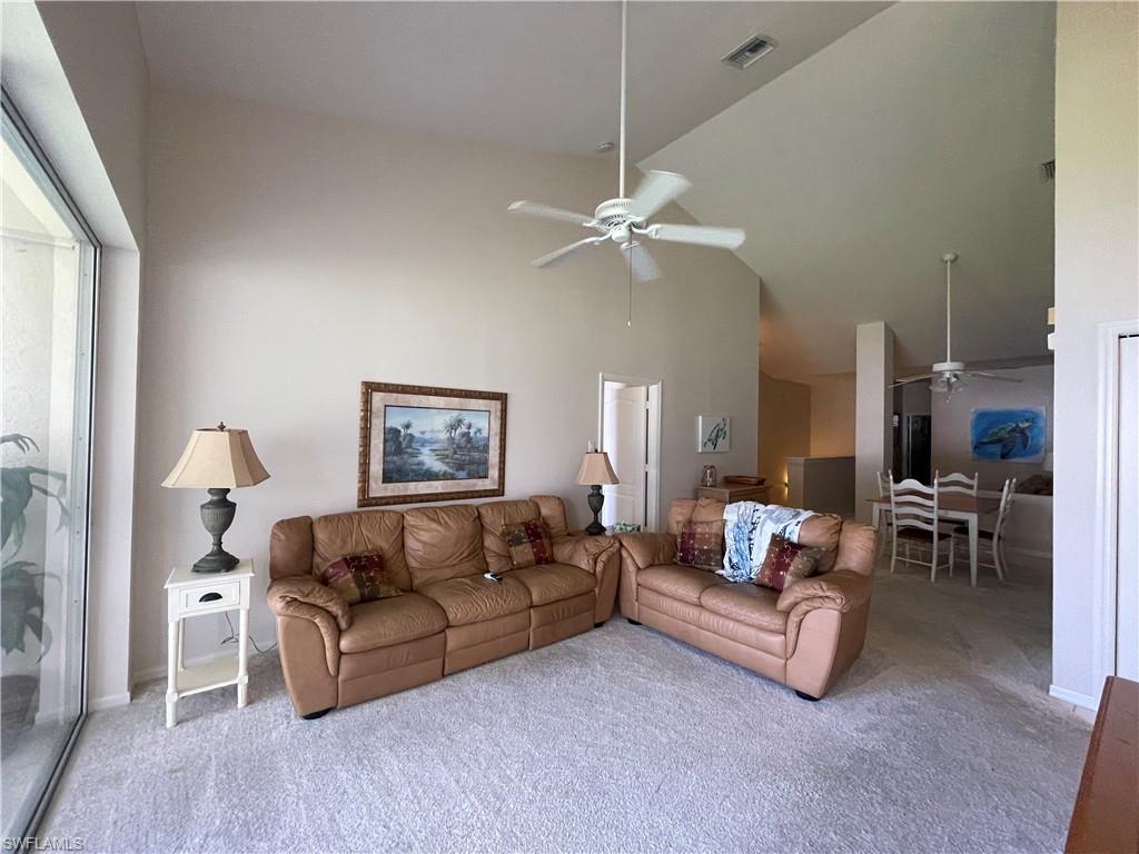Carpeted living room with high vaulted ceiling and a ceiling fan
