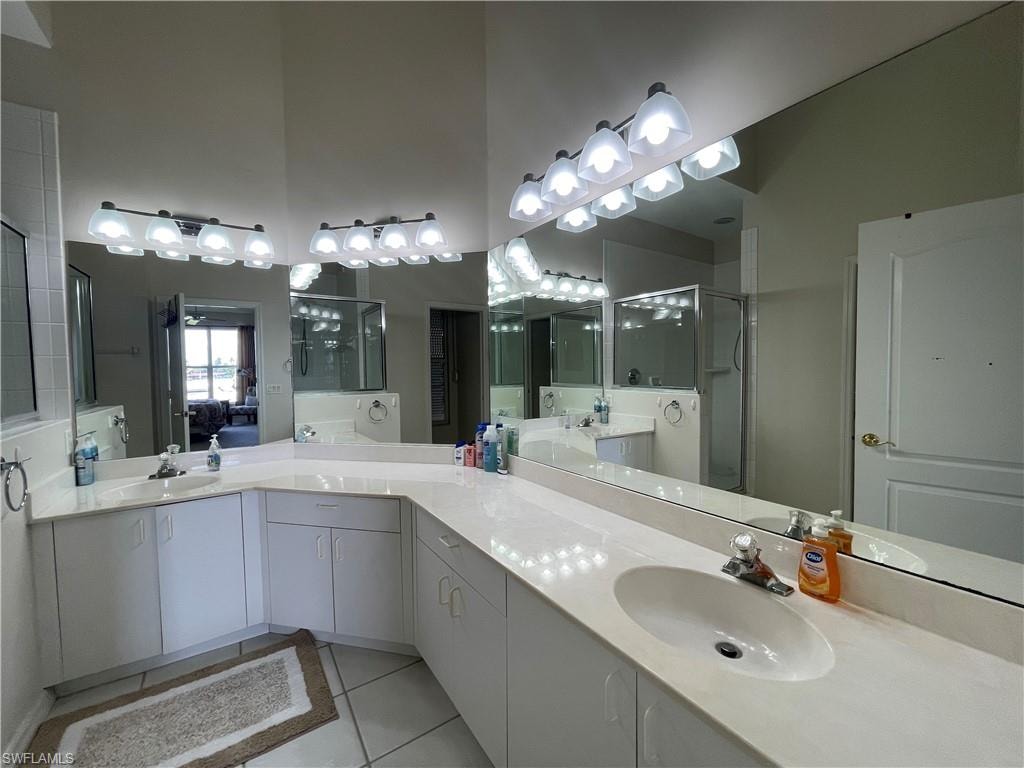 Ensuite bathroom featuring light tile patterned floors, a shower stall, two vanities, and a towering ceiling