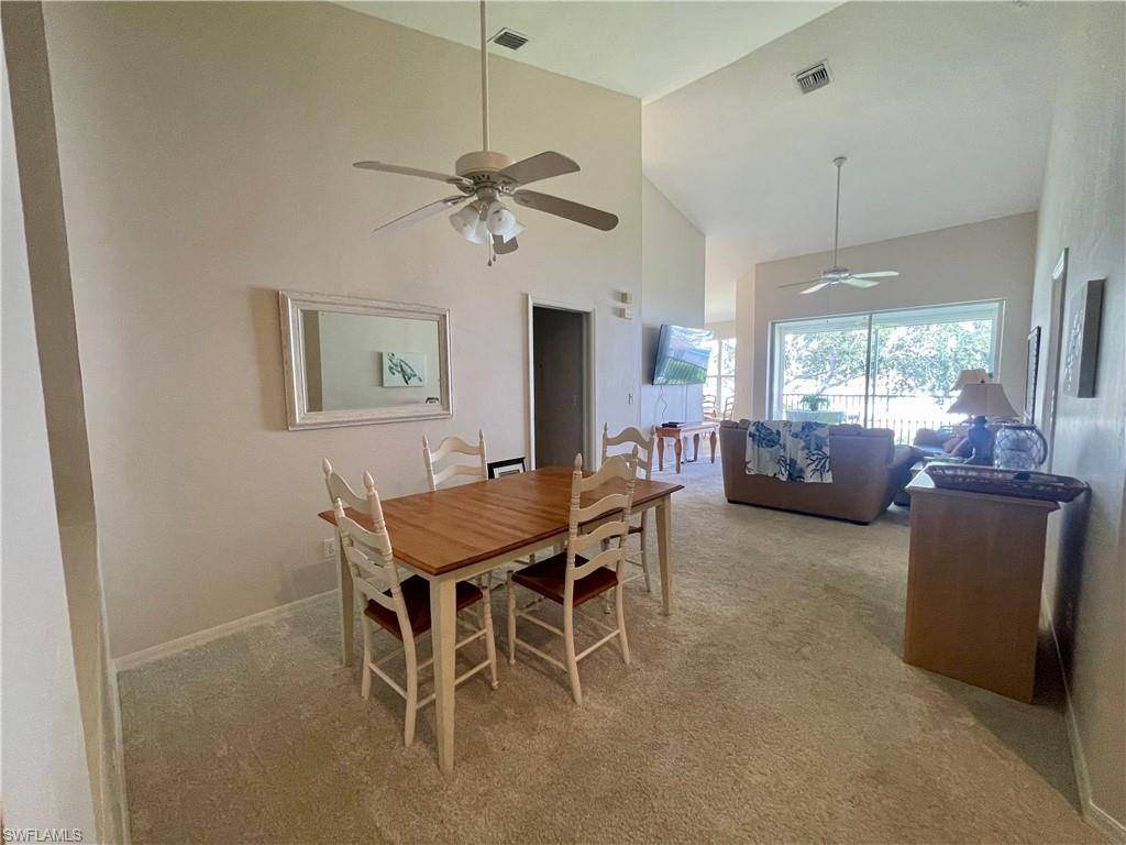 Dining area with high vaulted ceiling, light colored carpet, and a ceiling fan