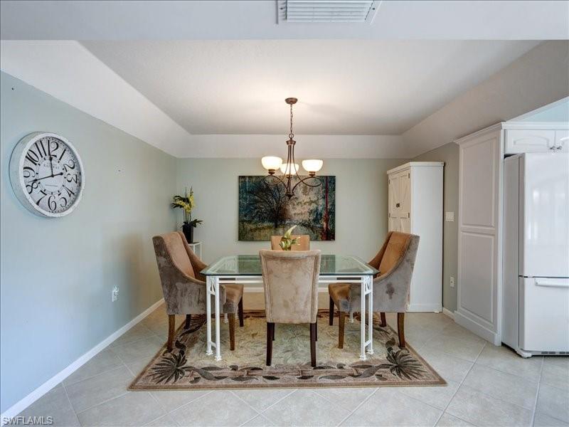 Dining space with light tile patterned flooring, a chandelier, and a raised ceiling