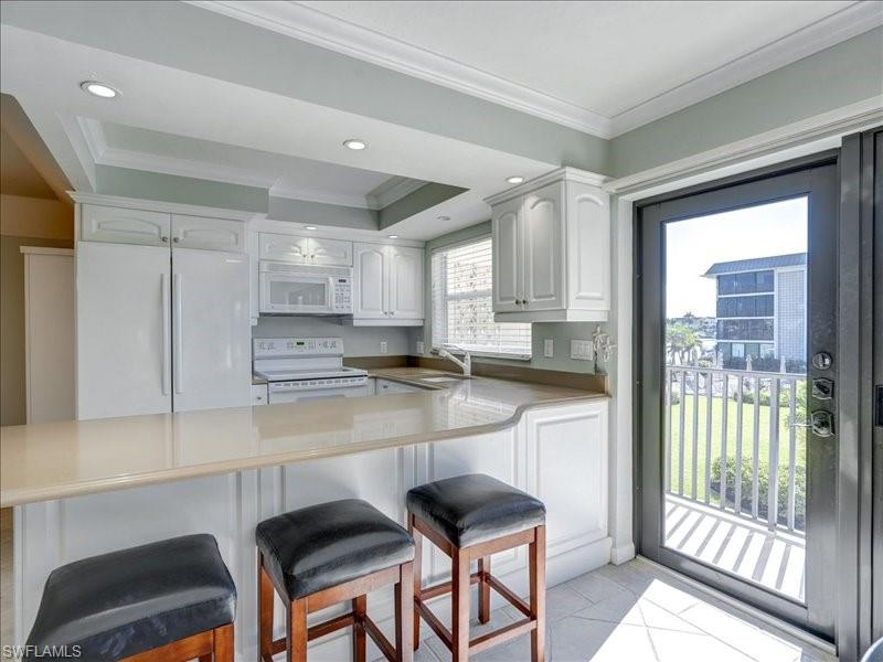 Kitchen featuring white appliances, a breakfast bar area, white cabinetry, crown molding, and recessed lighting