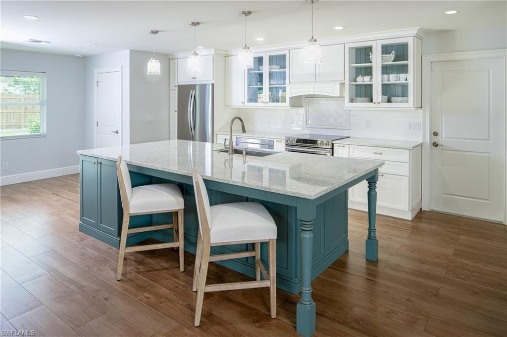 Kitchen featuring backsplash, glass insert cabinets, white cabinetry, light stone countertops, and a center island with sink