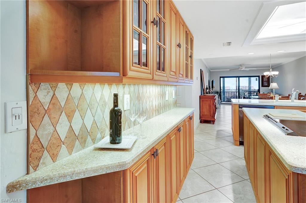 Kitchen with decorative backsplash, glass insert cabinets, light tile patterned floors, brown cabinets, and decorative light fixtures