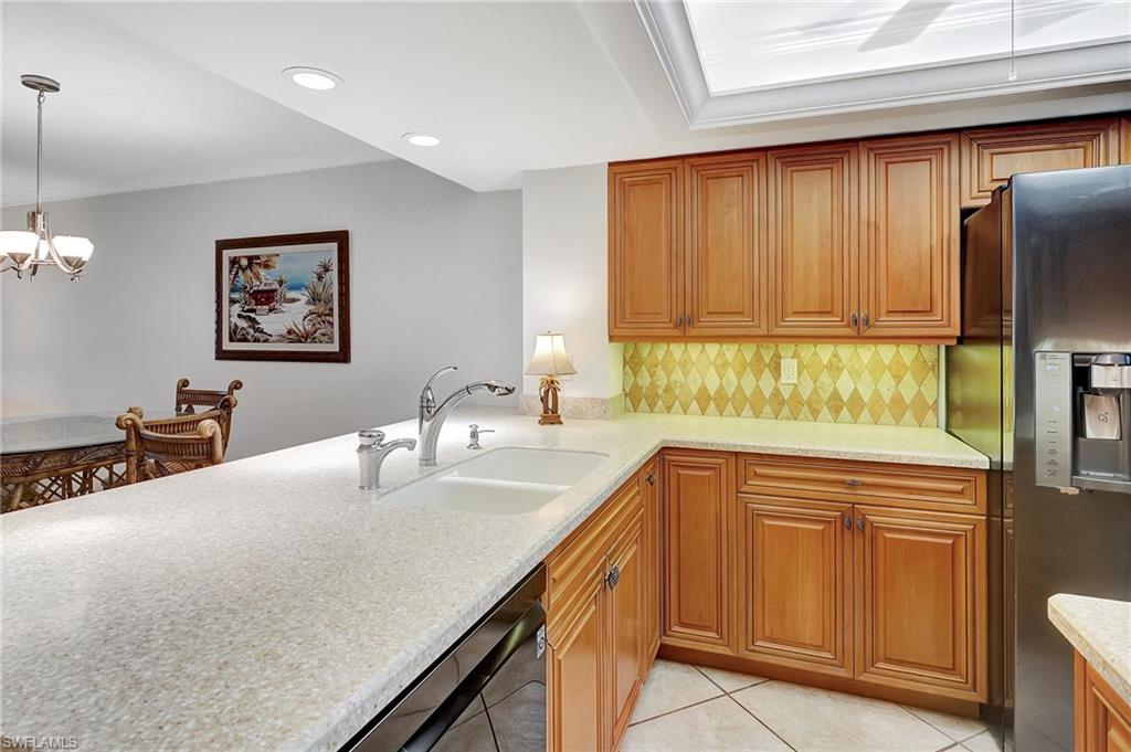Kitchen featuring backsplash, stainless steel fridge, light tile patterned flooring, brown cabinetry, and recessed lighting