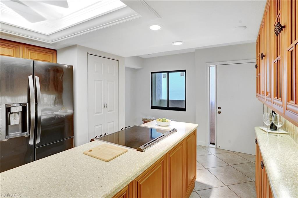 Kitchen with stainless steel fridge, recessed lighting, brown cabinetry, light tile patterned flooring, and black electric cooktop