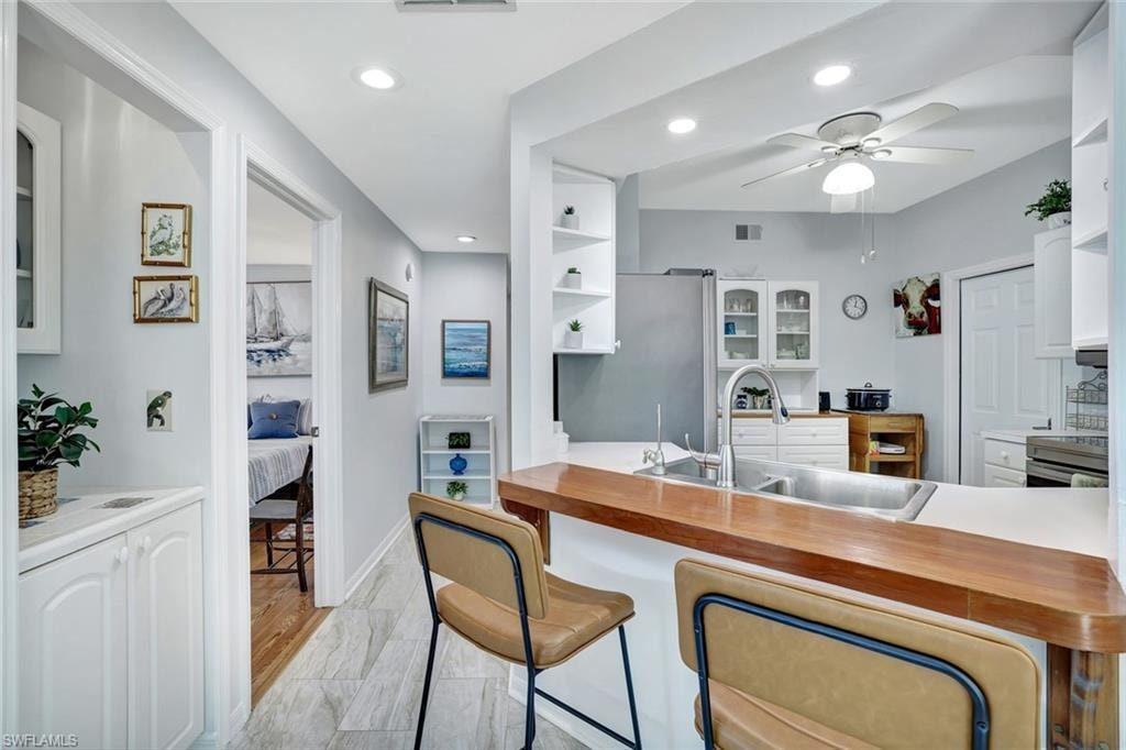 Kitchen featuring glass insert cabinets, open shelves, white cabinets, a breakfast bar, and appliances with stainless steel finishes
