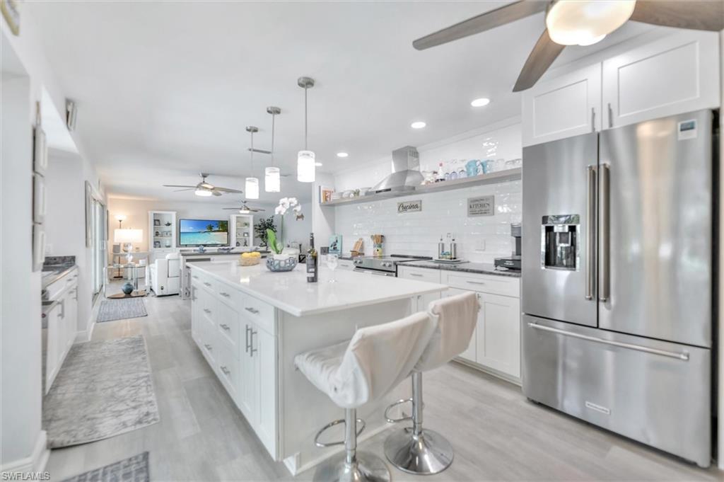 Kitchen with ceiling fan, appliances with stainless steel finishes, white cabinets, backsplash, and a kitchen bar