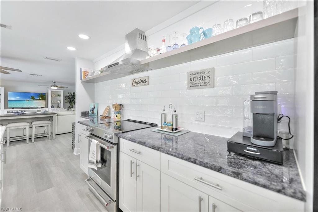Kitchen with stainless steel electric range, white cabinetry, dark stone counters, wall chimney exhaust hood, and decorative backsplash