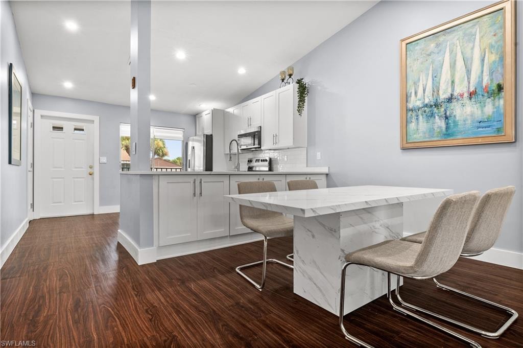 Kitchen featuring white cabinetry, decorative backsplash, lofted ceiling, a breakfast bar, and dark wood-style flooring
