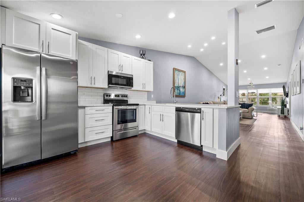 Kitchen with appliances with stainless steel finishes, open floor plan, white cabinets, lofted ceiling, and a peninsula